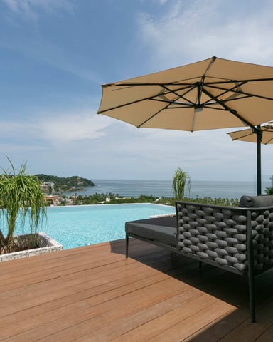 Rooftop infinity pool overlooking the ocean with lounge chairs and umbrellas on a wooden deck